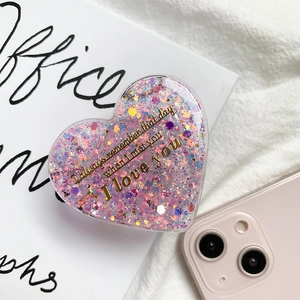 Close-up of heart-shaped glitter phone grip with gold text on white artistic book