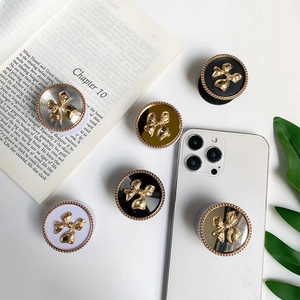 Detailed top view of gold bow phone grips with polished bead edges on a white desk