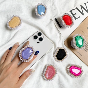 Collage of pearl-rimmed gemstone phone grips in eight colors on a white linen fabric