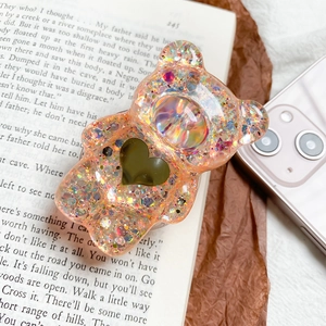 Dettaglio del supporto per telefono orso 3D con glitter su sfondo di libro aperto