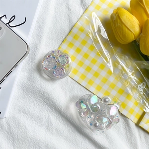 Macro shot of resin flower and butterfly phone grips with pearls on a white fabric background