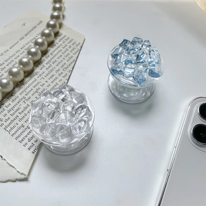 Detail of blue ice-cube folding phone grip stand next to pearl necklace and smartphone