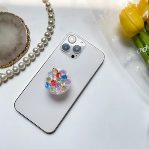 Close-up of a round clear phone grip filled with colorful faceted gems on a white smartphone
