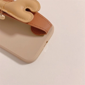 Détail de la coque iPhone beige avec dragonne en cuir et pendentif métallique rond