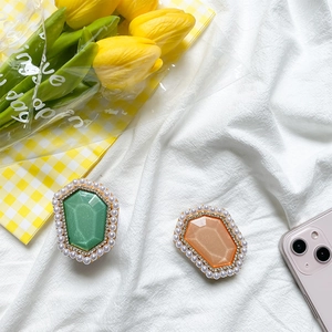 Detailed view of emerald and amber gemstone phone grips with pearl and rhinestone borders