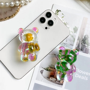 Detail of iridescent bear-shaped phone grip with embedded dried flowers and leaves