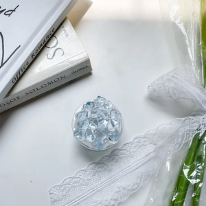 Close-up of a light blue crystal phone grip with foldable base on a minimal white desk