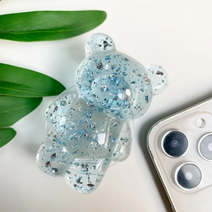 Detail of light blue resin bear phone grip with silver foil flakes on white surface