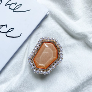Close-up of a luxury orange crystal phone grip with pearls and rhinestones on white fabric