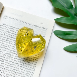 Macro shot of faceted yellow heart phone grip with silver flakes on an open book
