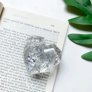 Macro detail of a 3D heart-shaped phone grip with silver foil flakes on an open book