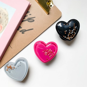 Macro shot of heart-shaped glitter phone grips with pearls on a minimalist desk