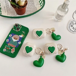 Detail view of cream white AirPods case featuring a green leather heart pendant and charm