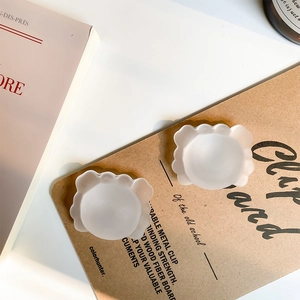 Translucent matte silicone nipple covers with wavy cloud edges on a minimalist board