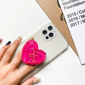 Pink heart-shaped liquid quicksand phone socket grip shown in use on a white smartphone