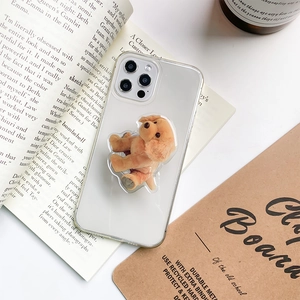 Close-up of a 3D plush puppy phone grip on a clear case over vintage books