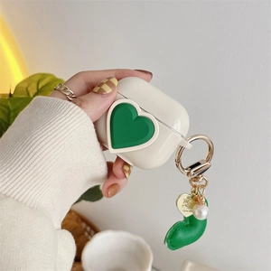 Detail view of cream AirPods case with 3D green heart and pearl lobster clasp accessory