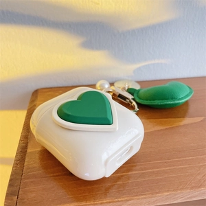 Detailed shot of white AirPods case with green heart and pearl charm on wood surface