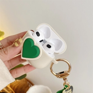 Detail view of cream AirPods silicone case featuring a 3D green heart and gold keychain