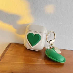 Close-up of cream AirPods case featuring a green 3D heart and luxury gold keychain