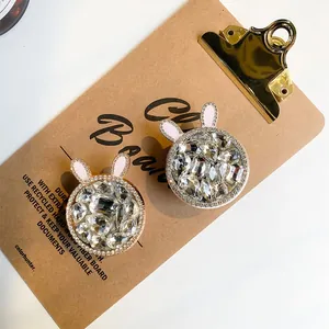Close-up of sparkling rhinestone bunny ear phone grips with pink enamel on a vintage board