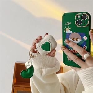 White AirPods case with green 3D heart and matching green cartoon character phone case