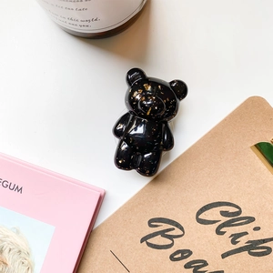 Close-up of a glossy black bear phone grip with gold foil flakes on a lifestyle background