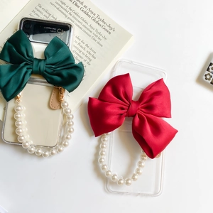 Detail of transparent phone case featuring a large satin bow and white pearl hand strap