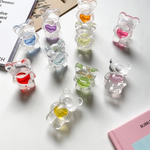Close-up of transparent acrylic bear phone grips with colorful hearts on white tabletop
