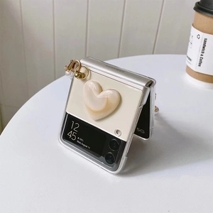 Detail of transparent Z Flip case with pearl chain and cream heart decor on white desk