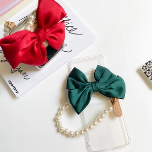 Detailed view of clear phone case featuring large satin bow and pearl bracelet strap