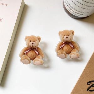 Close-up of cute acrylic brown bear phone grip with red checkered bow tie on white table