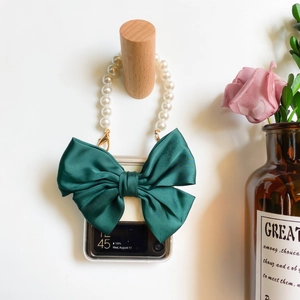 Detail of Galaxy Z Flip case with dark green bow and white pearl handle on wooden hook