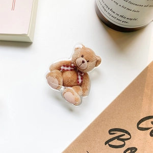 Detail of cute acrylic brown teddy bear phone grip with red bow on a white desk