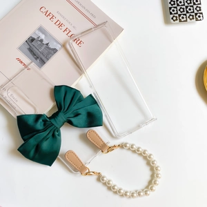 Detail of clear folding case with dark green satin bow and white pearl hand strap