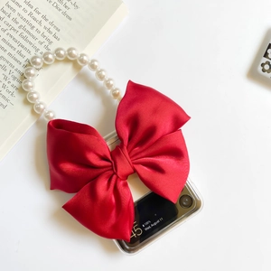 Detail of clear flip phone case with large red silk bow and elegant pearl hand strap