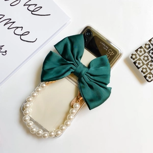 Close-up of clear phone case with a dark green silk bow and a large pearl wrist strap