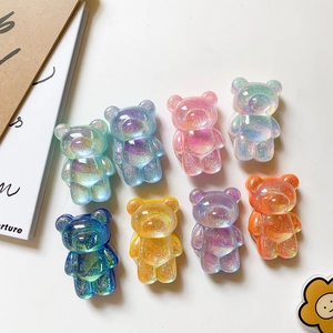 Flat lay macro of eight colorful glittery resin bear phone grips on a white desk