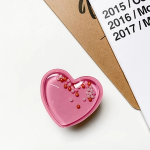 Soporte de móvil corazón rosa con purpurina y cuentas naranjas y blancas sobre fondo blanco