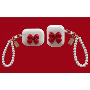 Detail of white AirPods case featuring a red 3D bow and elegant pearl strap accessory