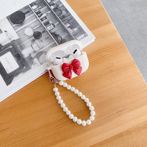 Detail of AirPods Pro case with red bow and elegant pearl strap on wooden background