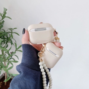 Glossy beige AirPods case with elegant white pearl lanyard and gold metal clasp