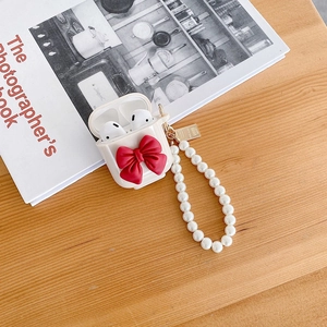 Close-up of AirPods case featuring a large red bow and an elegant pearl chain accessory