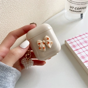 Dettaglio custodia AirPods con fiocco arancione a pois e ciondolo a cuore in perla