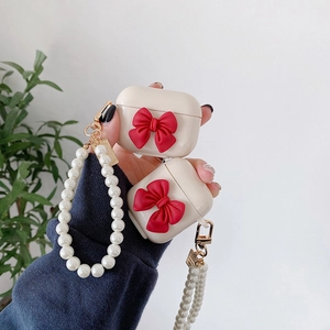 Detail of cream AirPods case with a red 3D bow and elegant pearl chain accessory