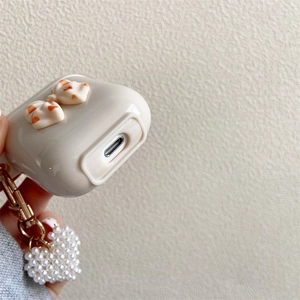 Dettaglio custodia AirPods crema con fiocco 3D e ciondolo a cuore con perle