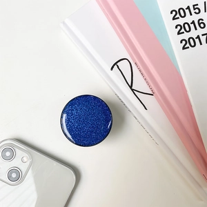 Close-up of a blue glitter phone socket grip placed on books in a lifestyle setting
