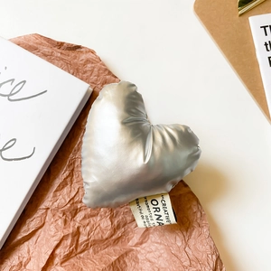 Silver heart-shaped puffy phone grip accessory with metallic finish and fabric tag
