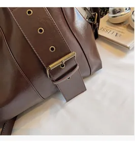 Detail of dark brown glossy leather tote with vintage brass buckle and matte texture