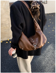 Close-up of brown leather crossbody bag featuring silver star rivets and metal hook closure